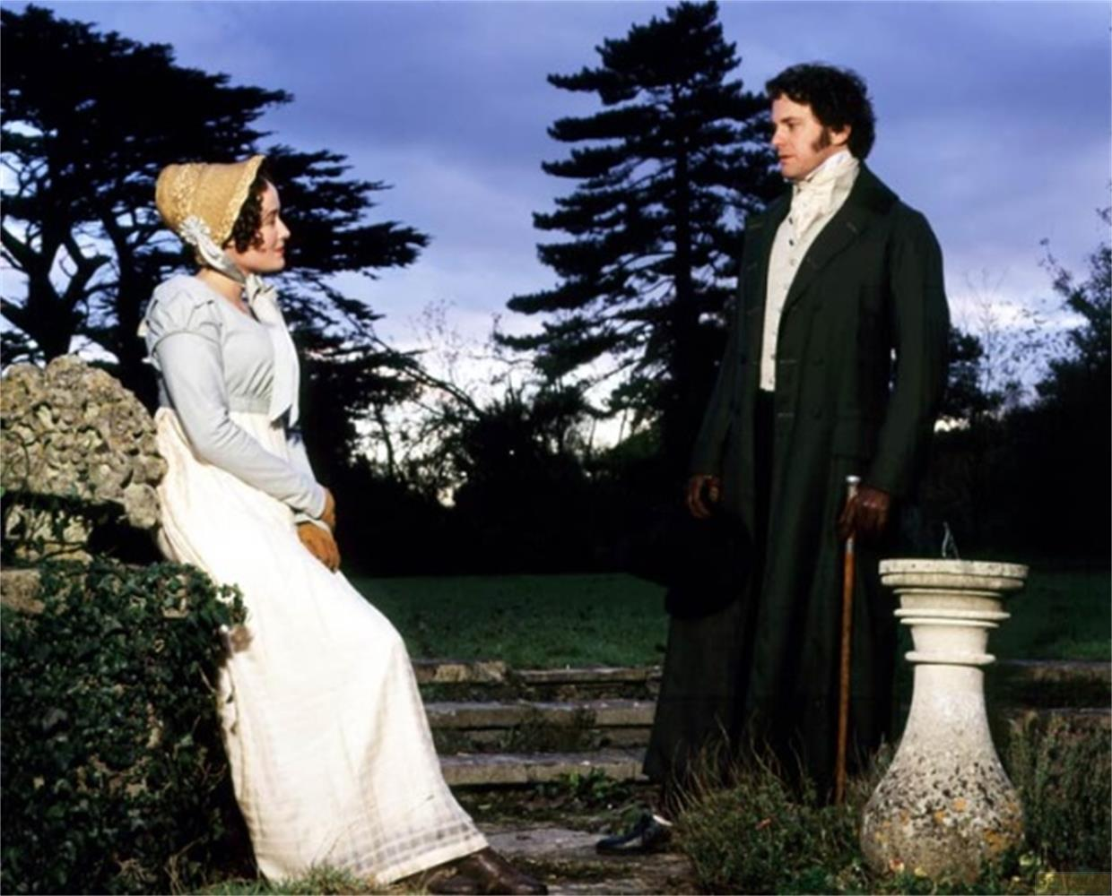 Homme en long manteau vert et femme en robe claire debout dehors.
