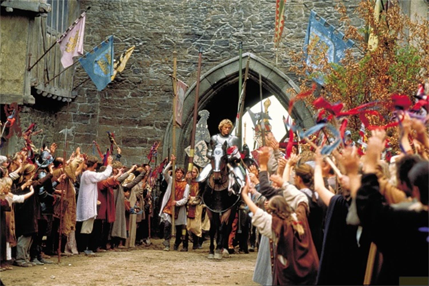 Un chevalier à cheval est accueilli par une foule en liesse avec des drapeaux.