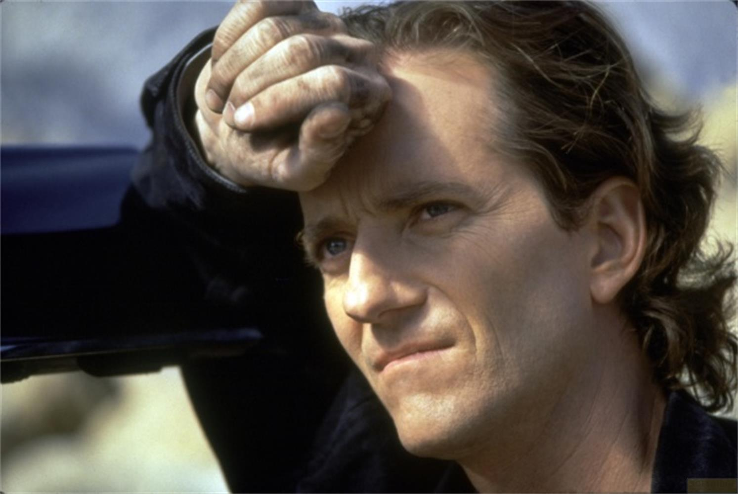 Un uomo con capelli castani appoggia la testa sulla mano, guardando a destra.