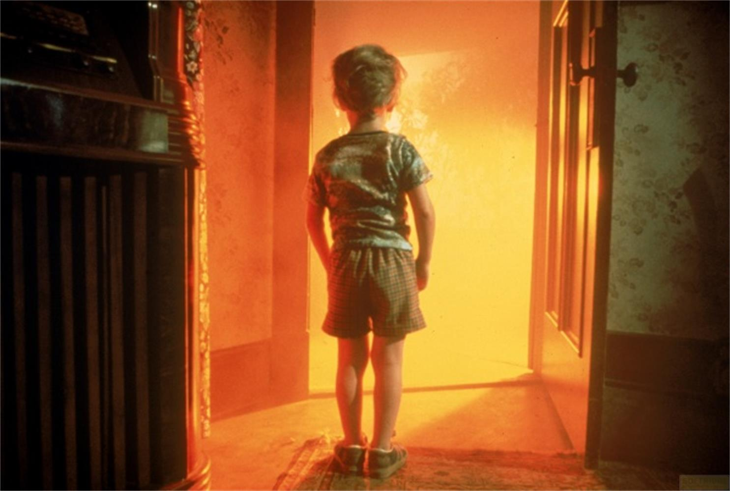 Un garçon se tient devant une lumière vive brillant à travers une porte.