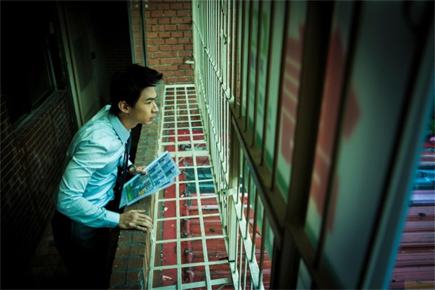 Un uomo in camicia blu sta vicino a un muro di mattoni tenendo un giornale.