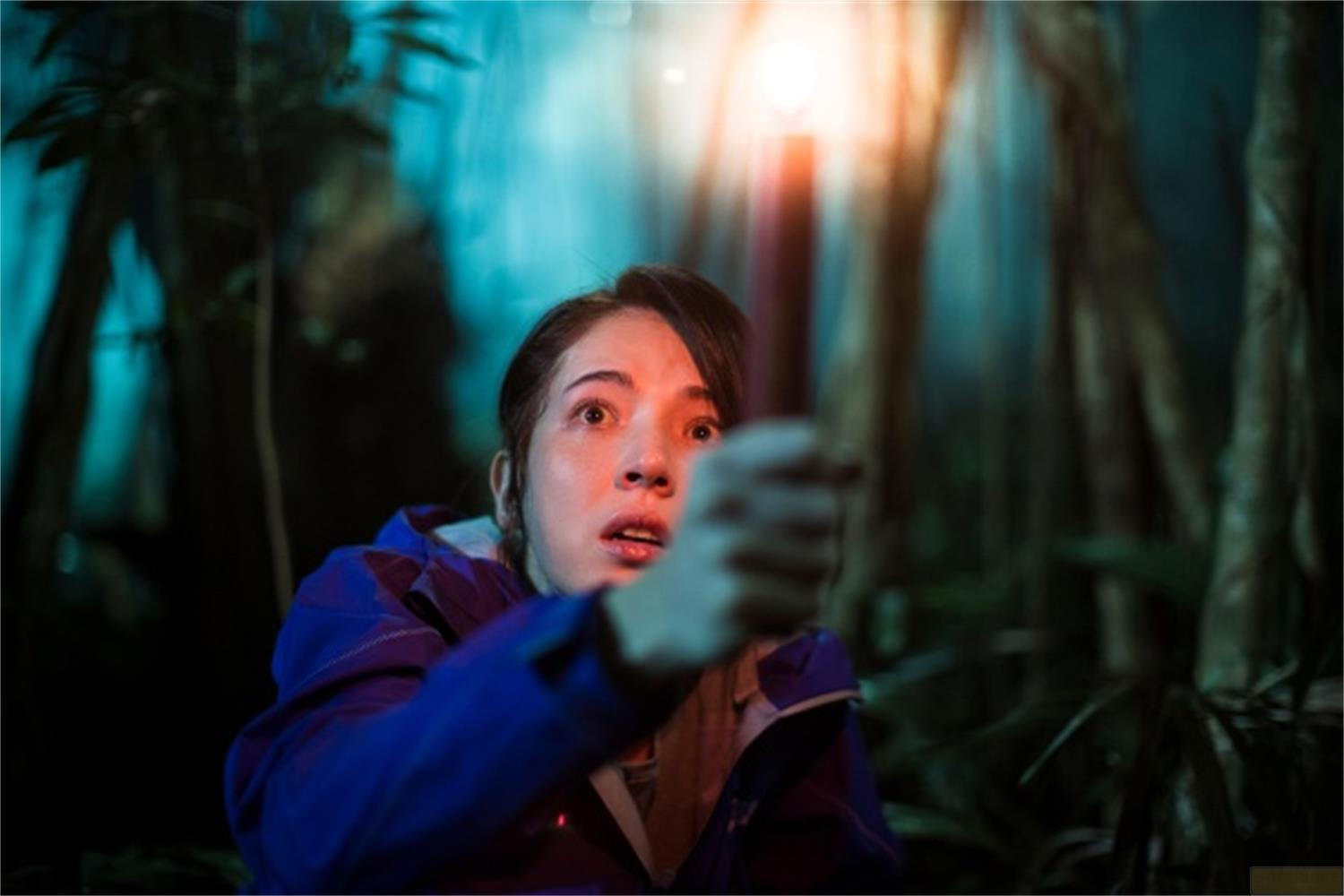Una donna in giacca blu tiene una candela accesa in una foresta oscura.