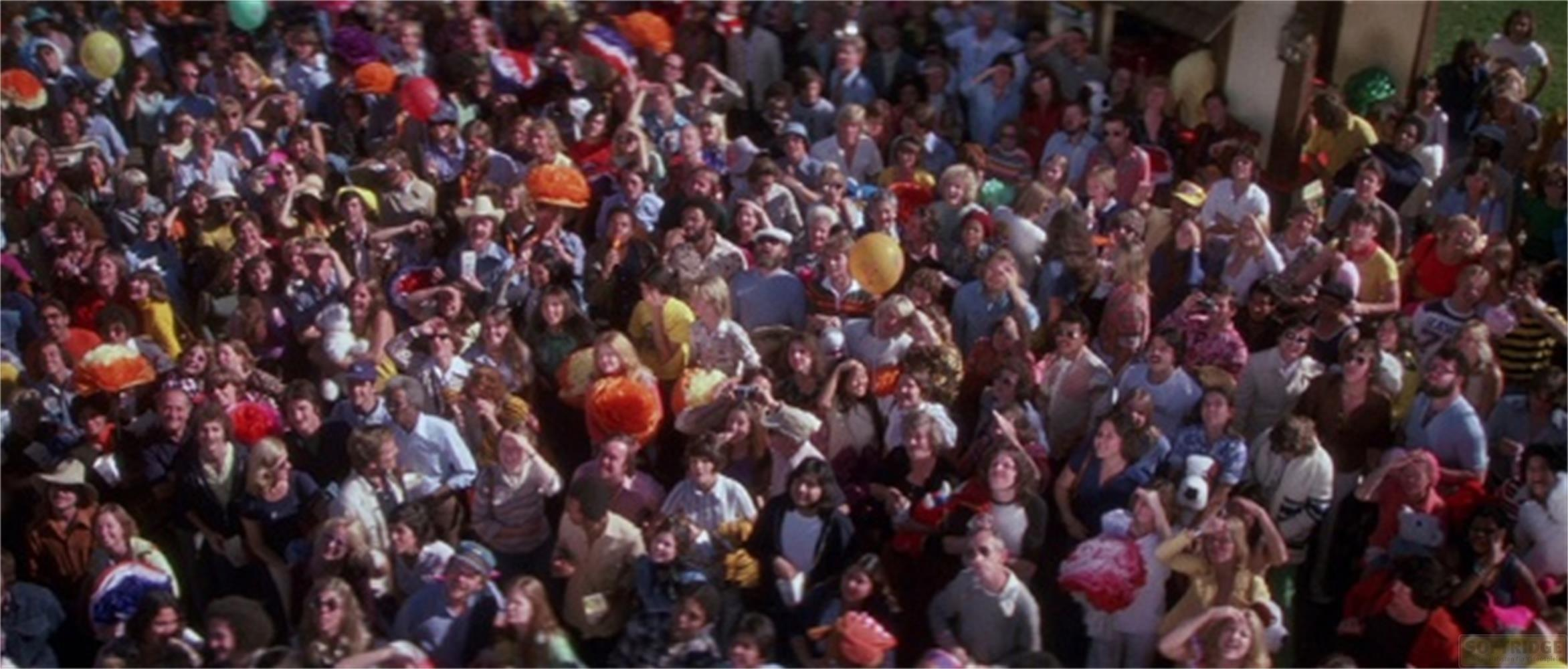 Eine große Menge Menschen in bunter Kleidung, einige halten Luftballons.