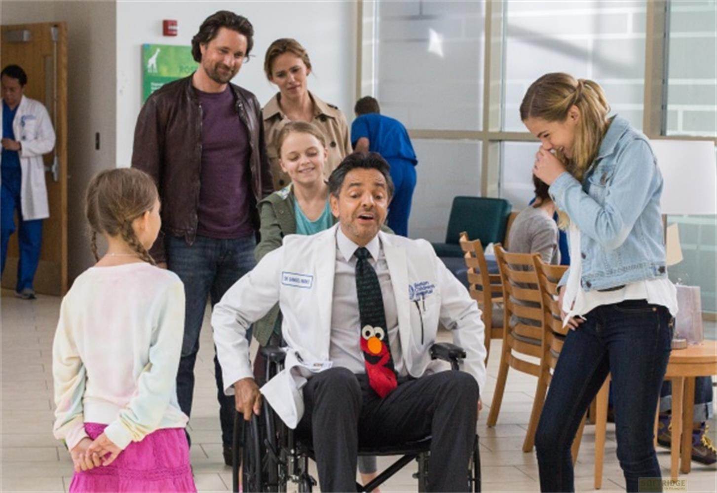 Ein Mann im Rollstuhl mit Elmo-Krawatte, umgeben von Familienmitgliedern und Krankenhauspersonal.
