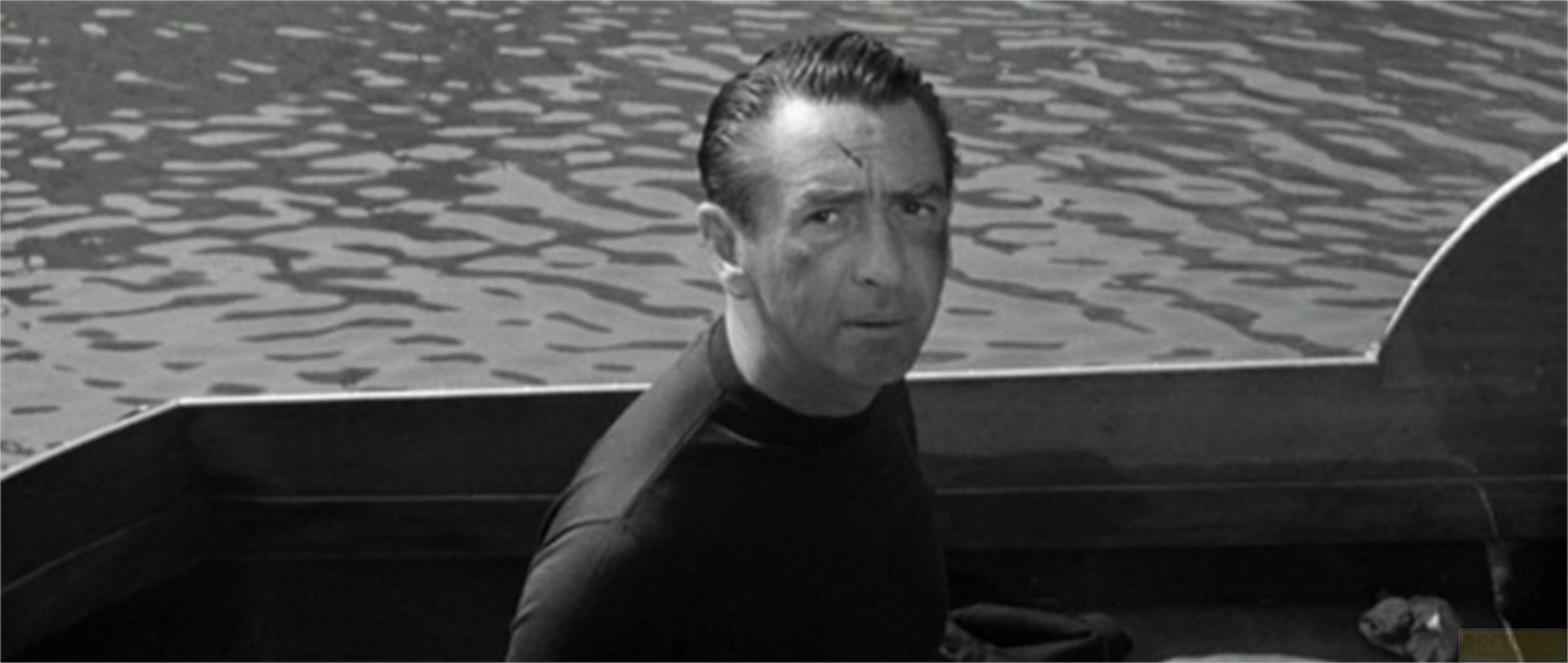 Un homme en chemise sombre est assis dans un bateau sur l'eau.