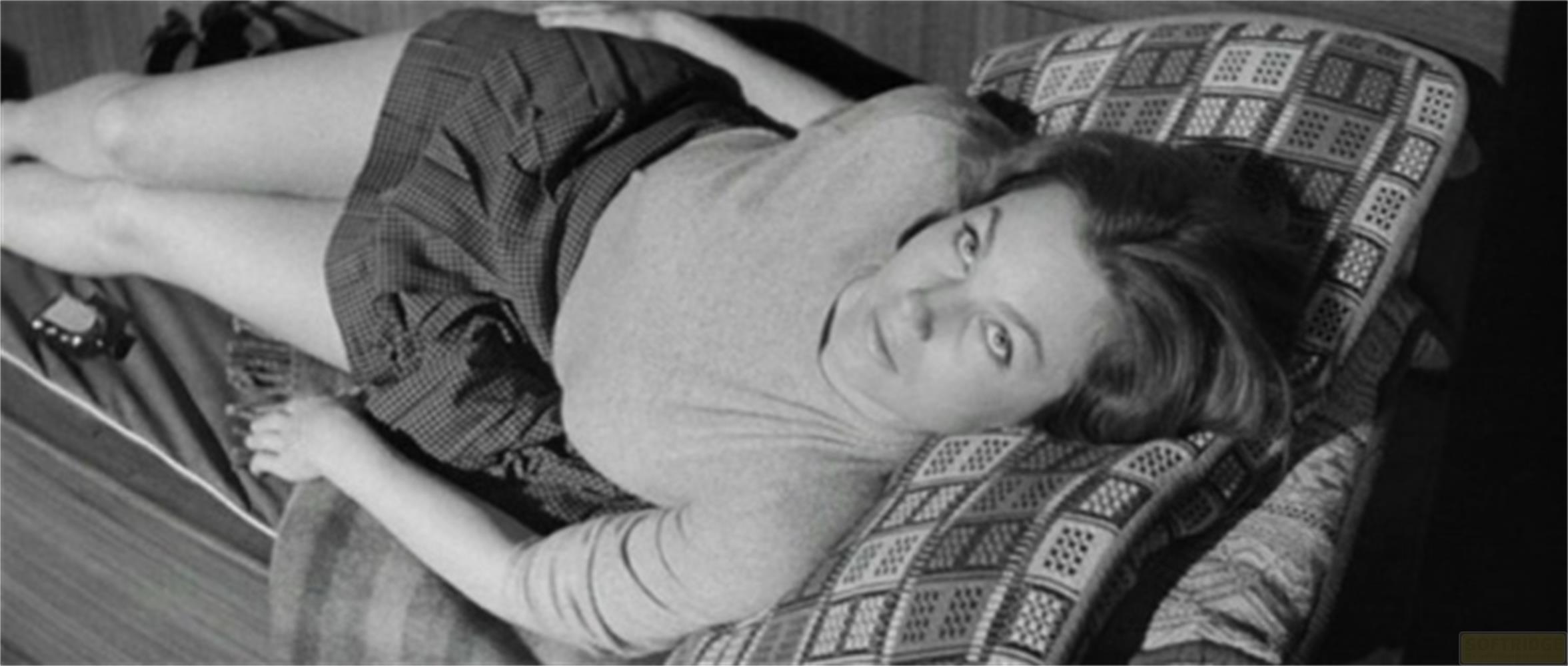 Une femme est allongée sur un lit, portant une robe et regardant vers le haut.