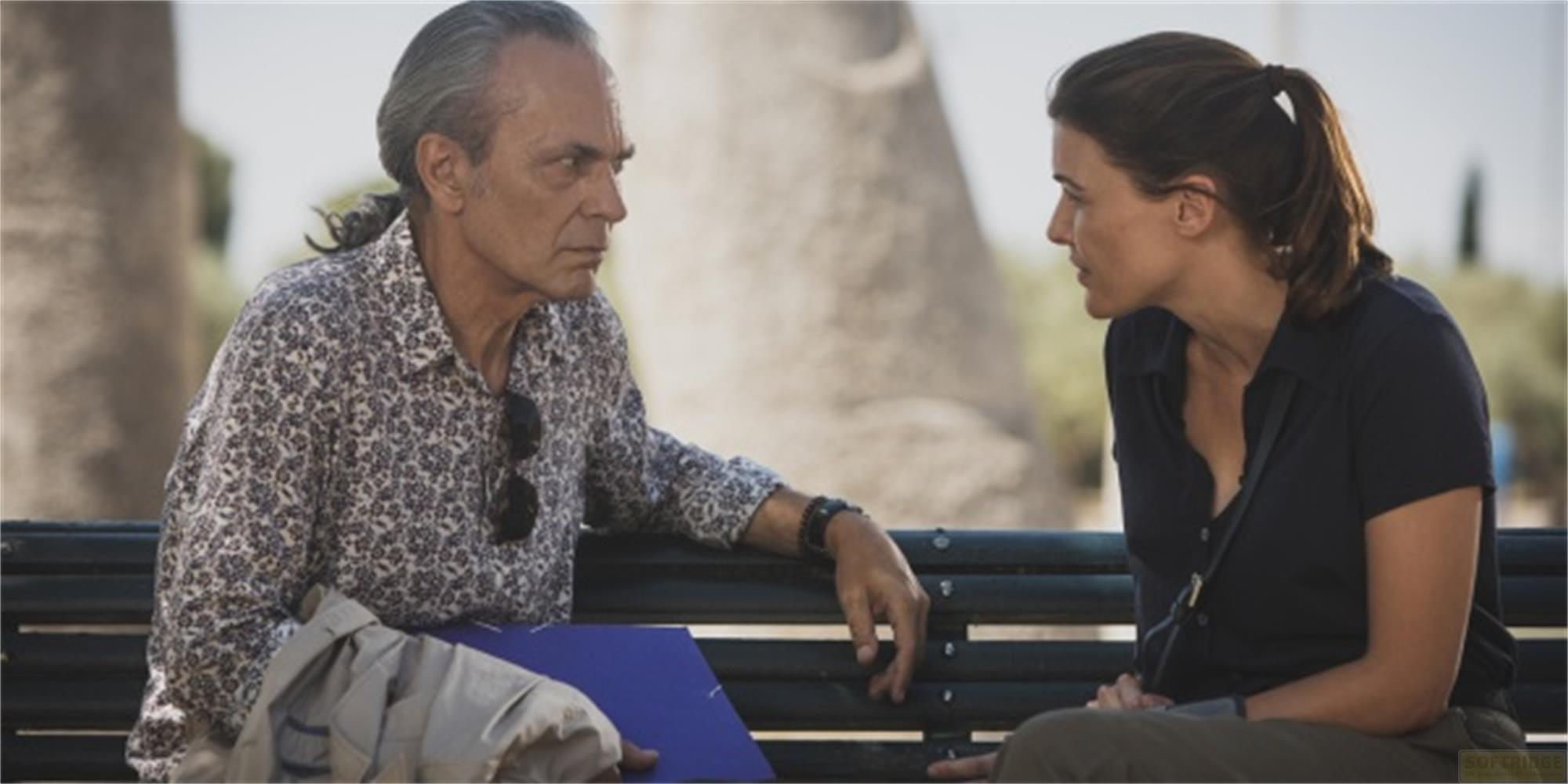 Un uomo e una donna siedono su una panchina, parlando all'aperto.