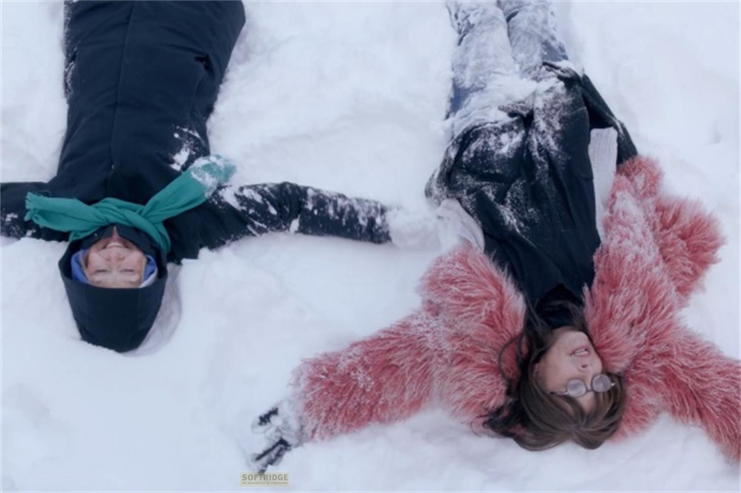Due donne sdraiate sulla neve, una in nero con sciarpa turchese, l'altra in rosa.