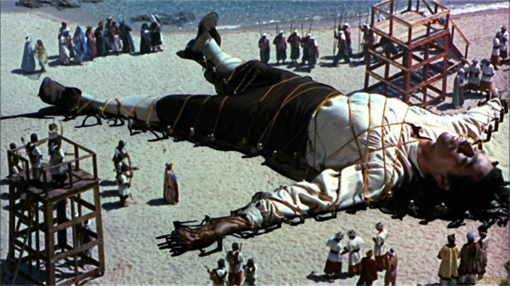 Un homme géant, ligoté, gît sur une plage de sable entouré de nombreuses personnes.