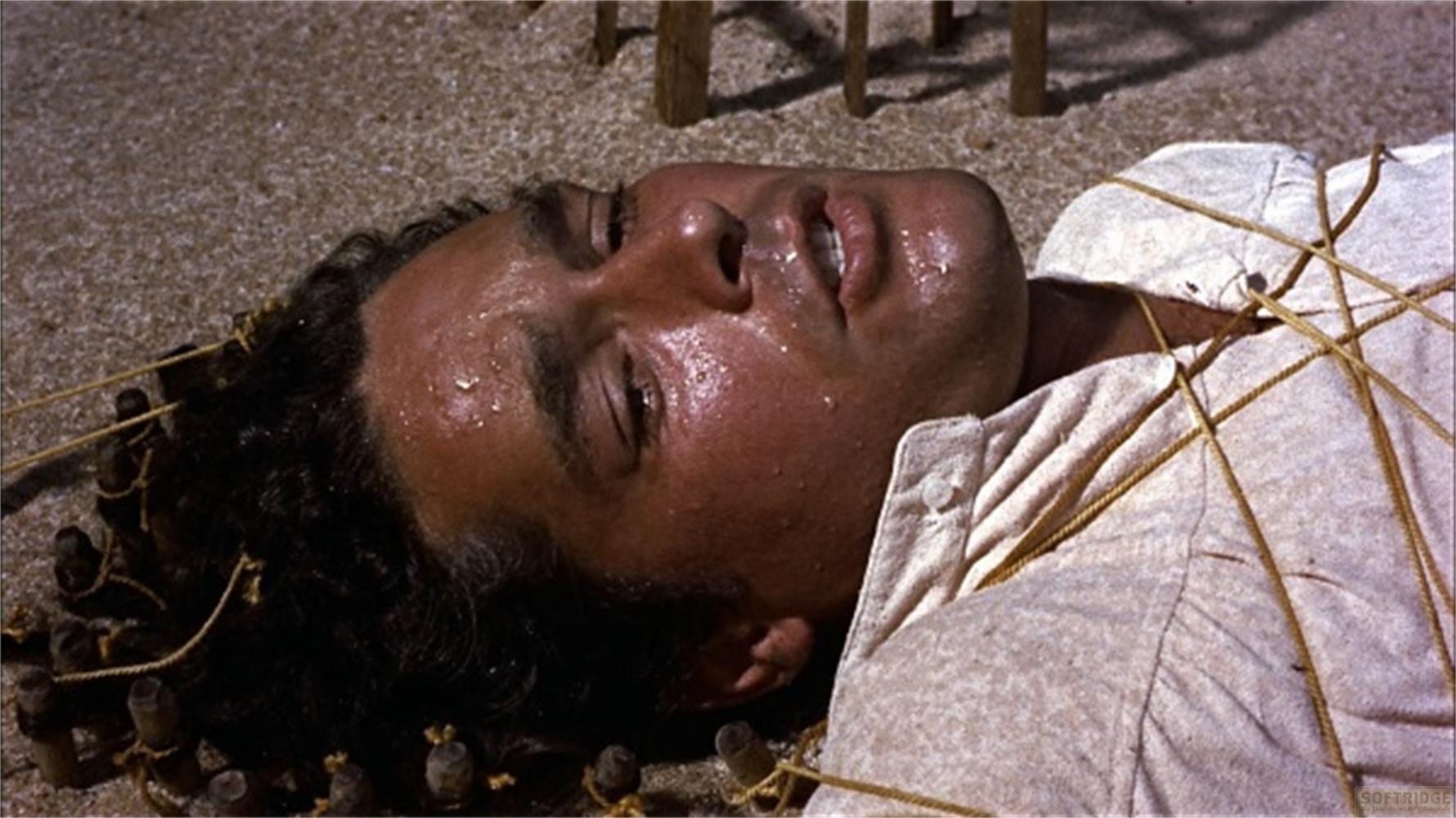 Homme allongé au sol, attaché avec des cordes, en sueur.