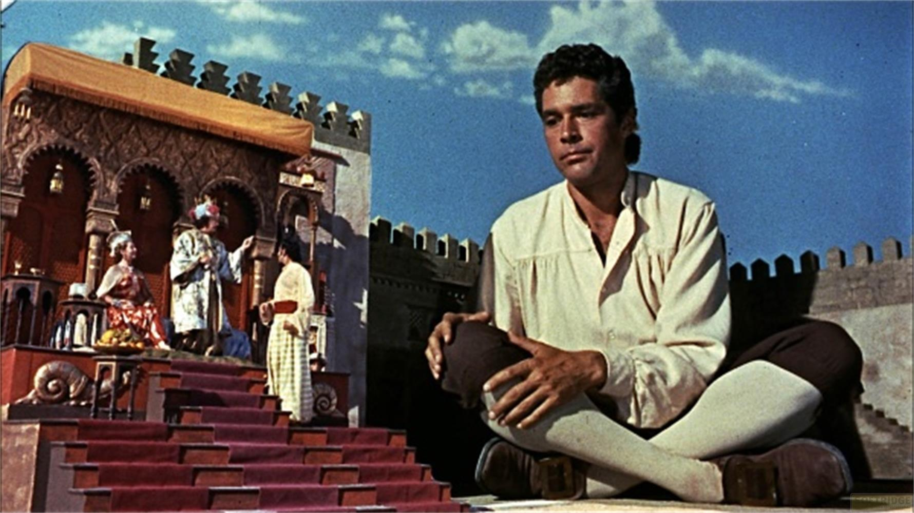 Un homme est assis devant une scène orientale avec des interprètes et de l'architecture.