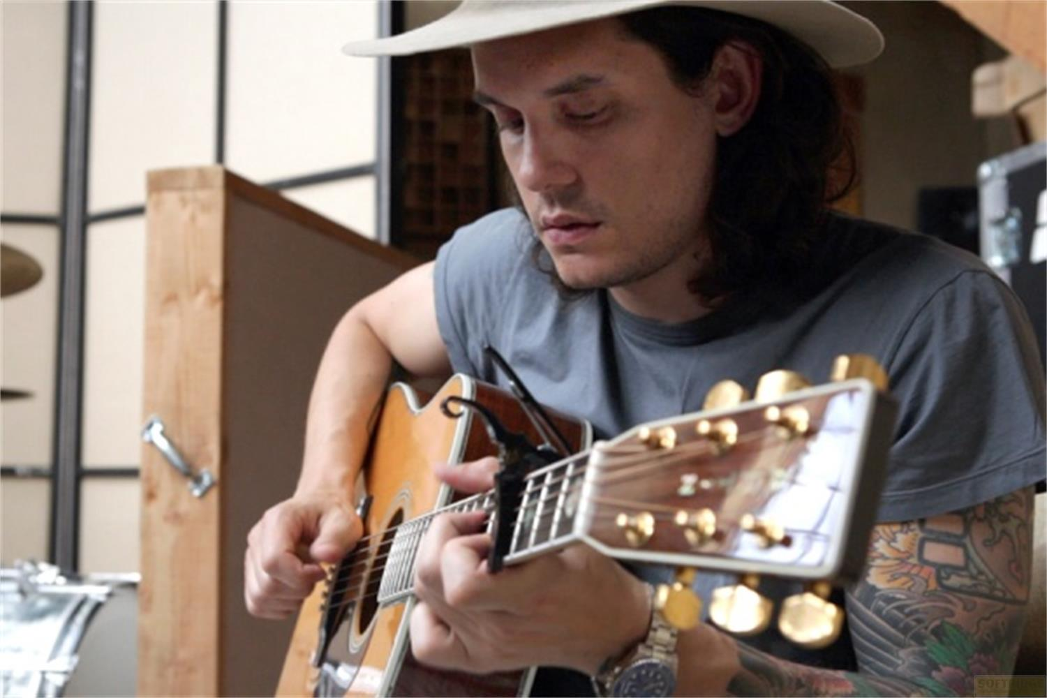 Uomo con cappello suona chitarra acustica in studio.