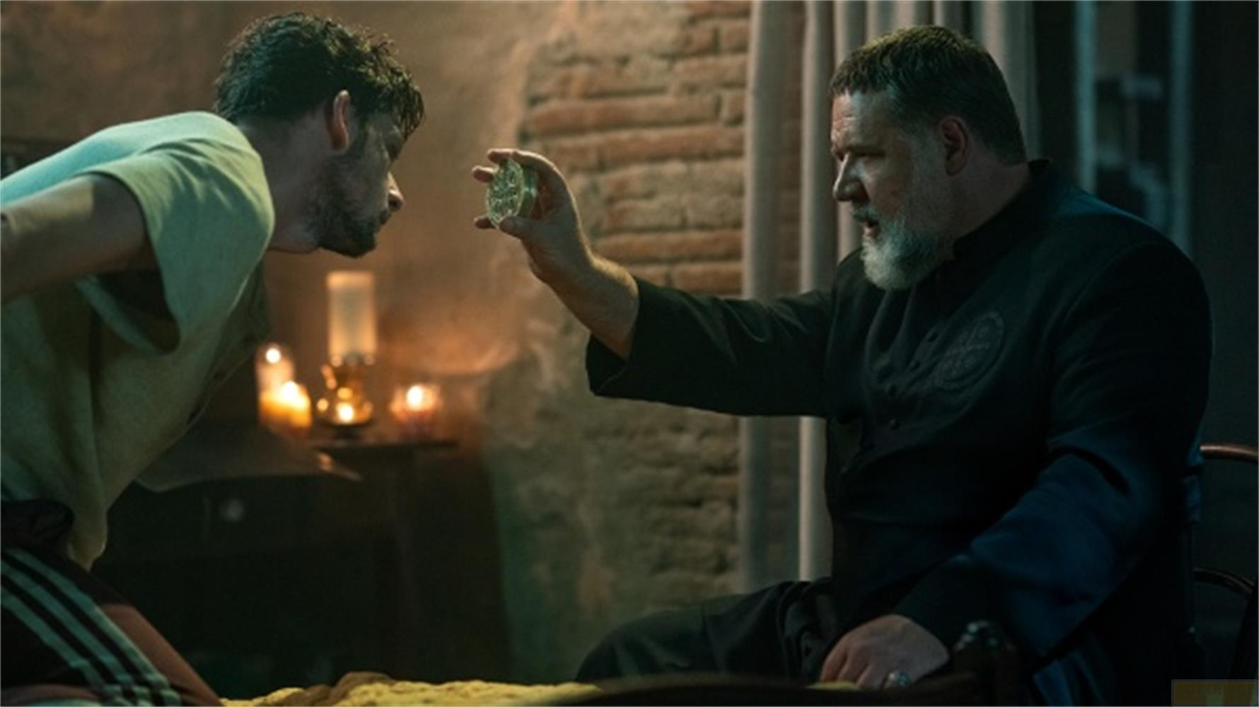 Un uomo barbuto tiene un oggetto di vetro, un altro uomo guarda.