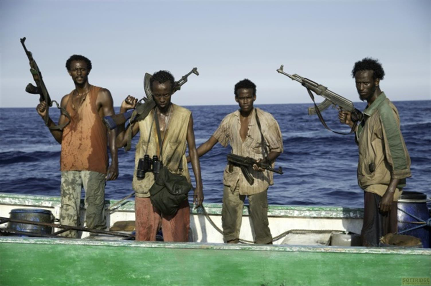 Quatre hommes armés dans un bateau en mer. L'un tient un fusil; deux portent des sacs à dos.
