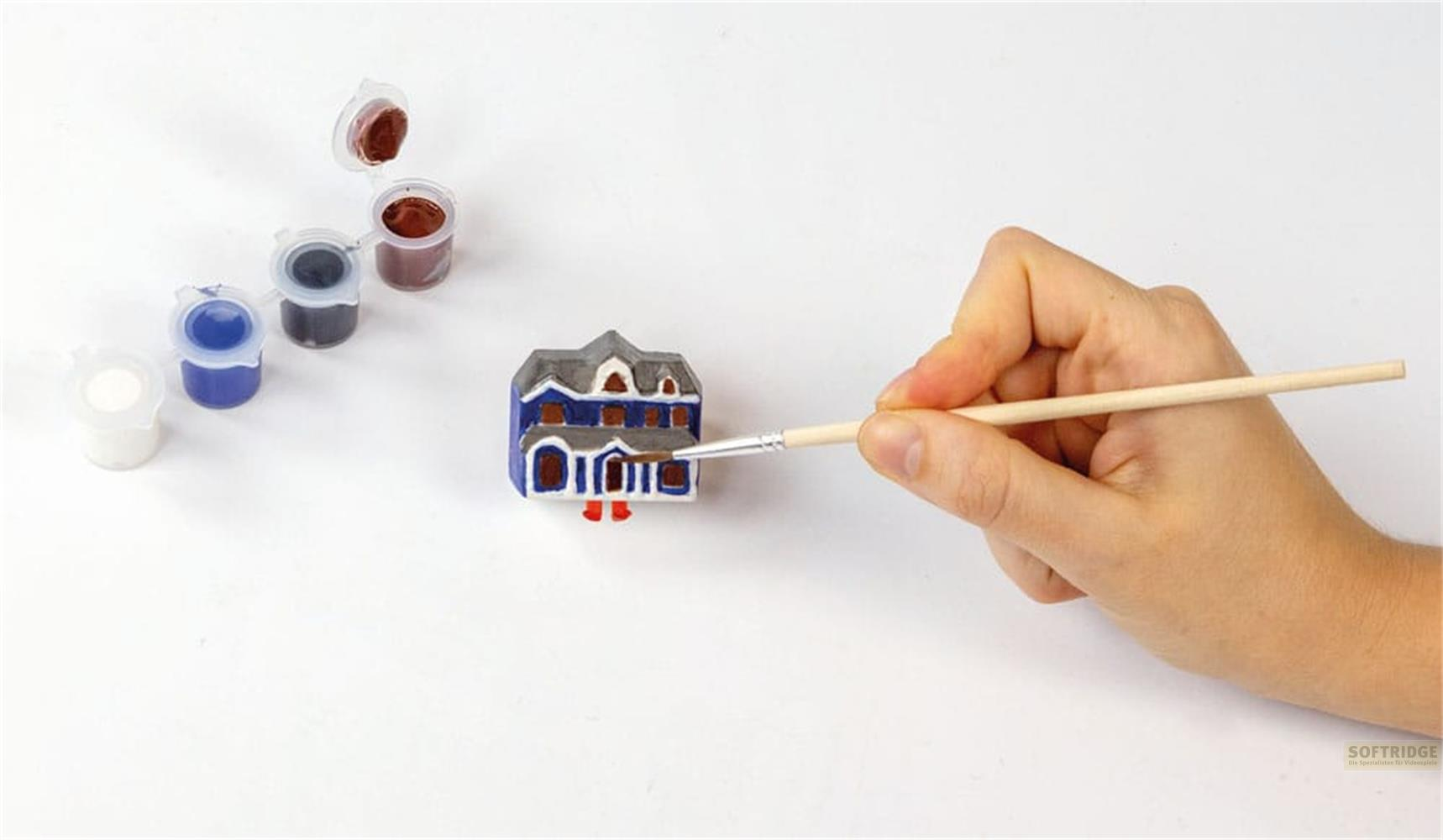 Mano pinta una casa modelo azul y gris con pincel y botes de pintura.