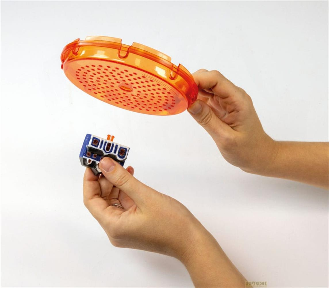 Manos sostienen un objeto azul y un disco naranja perforado.