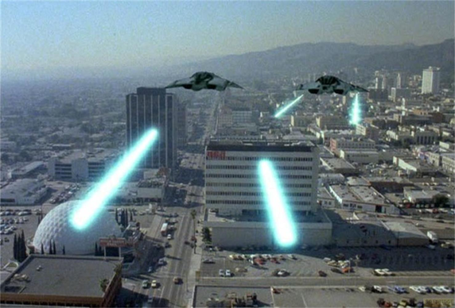 Due velivoli futuristici sparano raggi blu su uno skyline cittadino.