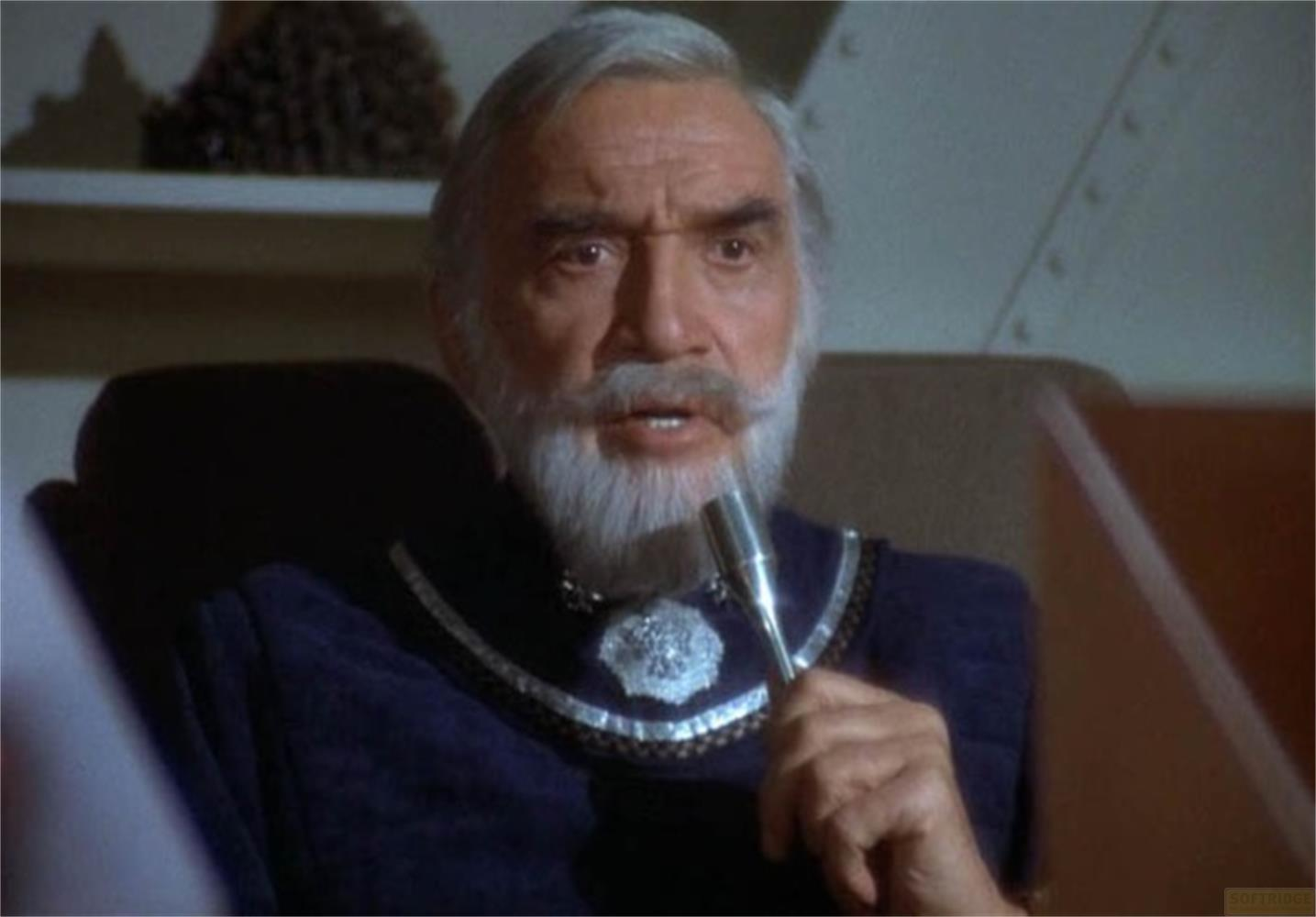 Un uomo anziano con capelli e barba grigi tiene un microfono.
