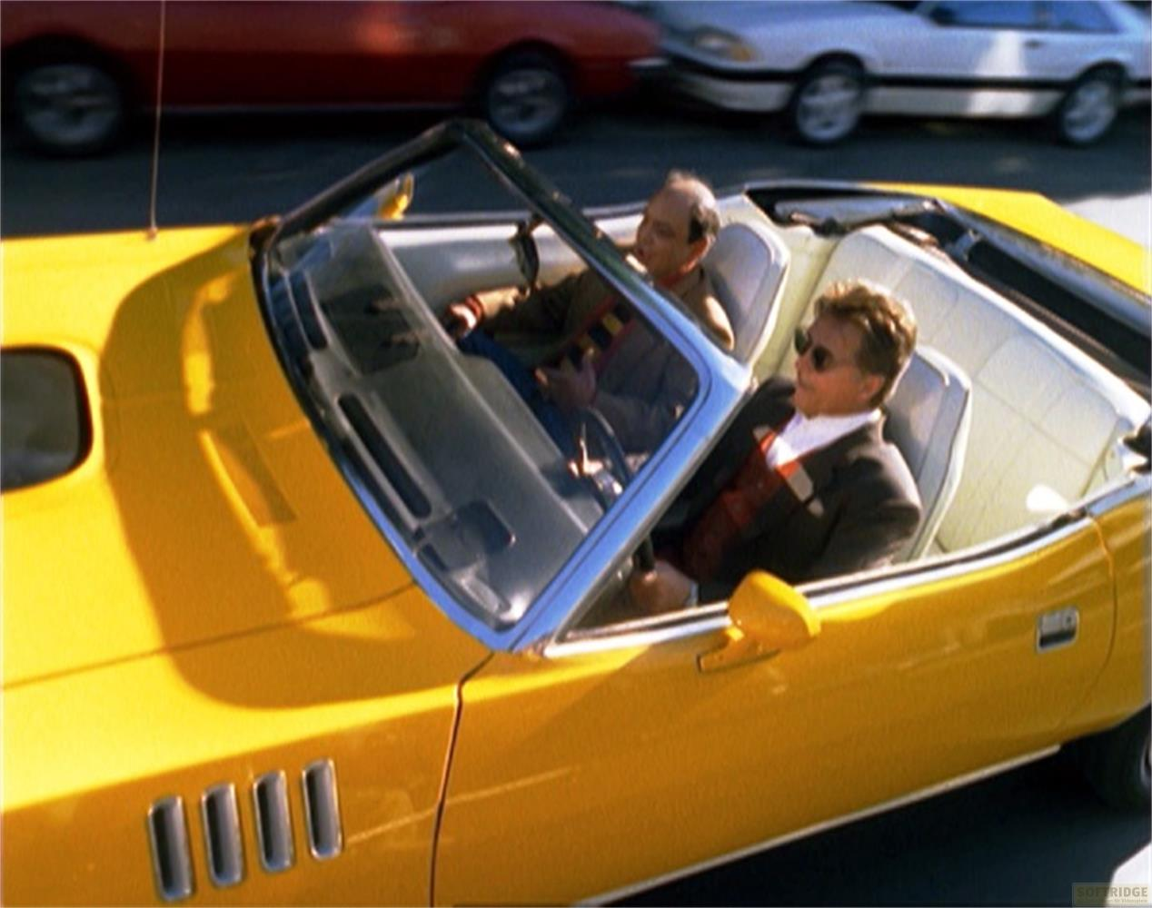 Due uomini in una convertibile gialla con interni bianchi stanno guidando.