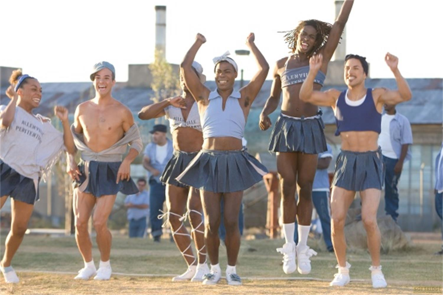 Cinq hommes en jupes de pom-pom girl et débardeurs sautent joyeusement dehors.