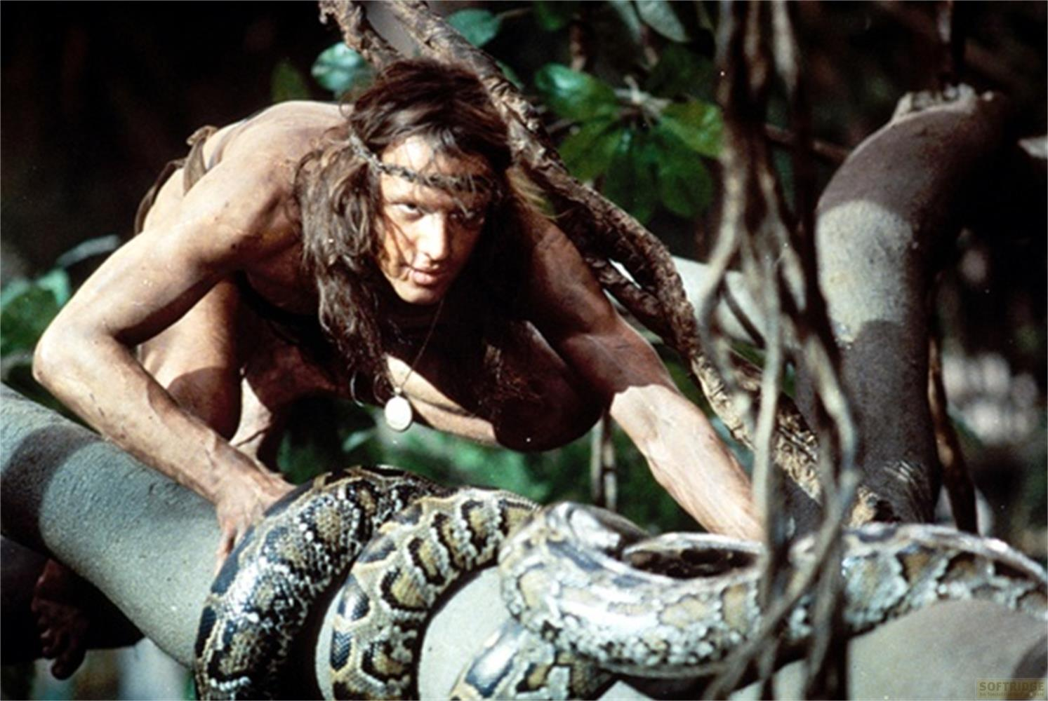 Un uomo si arrampica su un tronco d'albero, circondato dalla giungla e da un serpente.