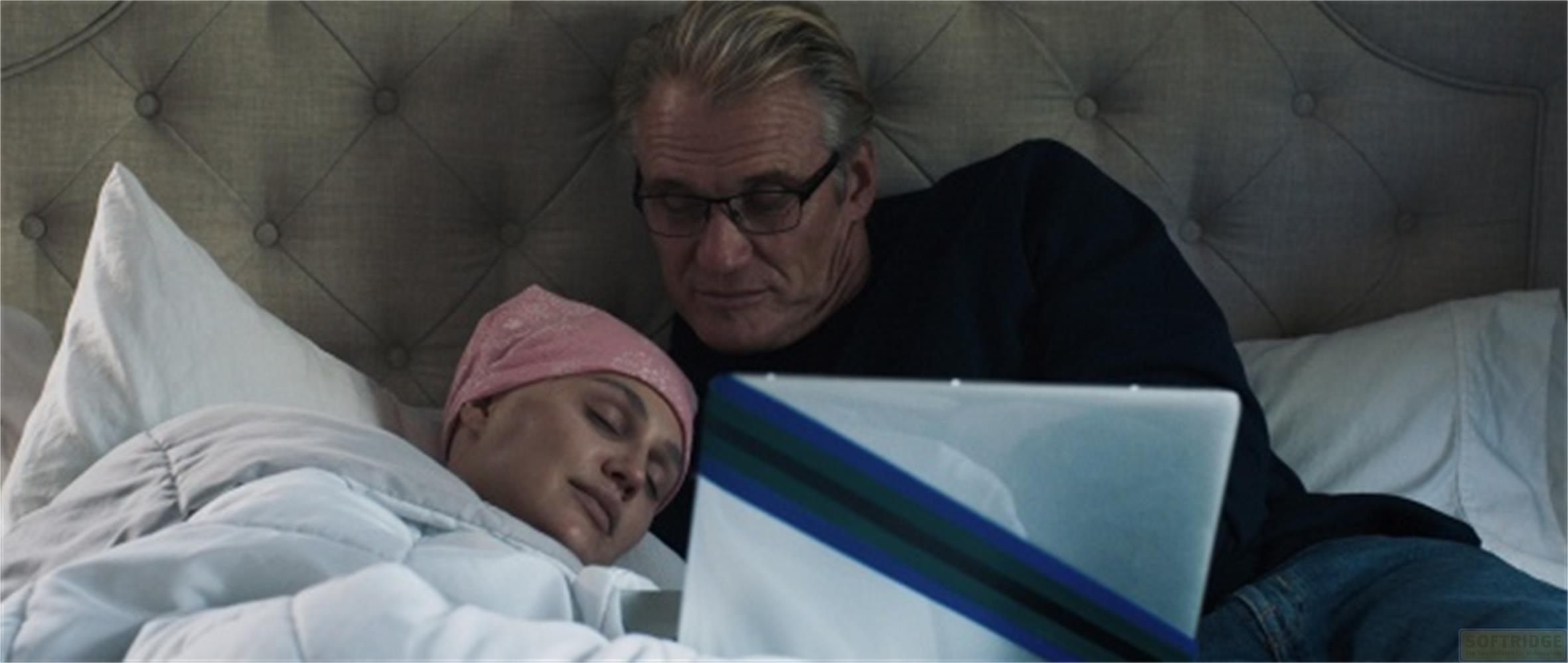 Uomo guarda laptop mentre donna con cappello rosa dorme.