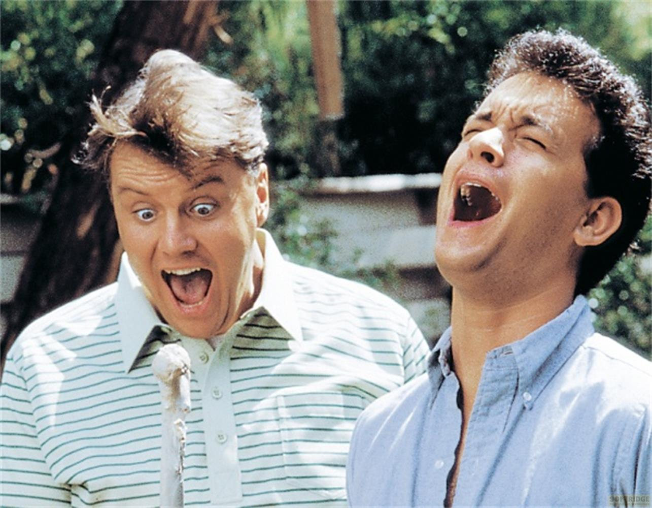Deux hommes rient bouche bée à l'extérieur, entourés de verdure.