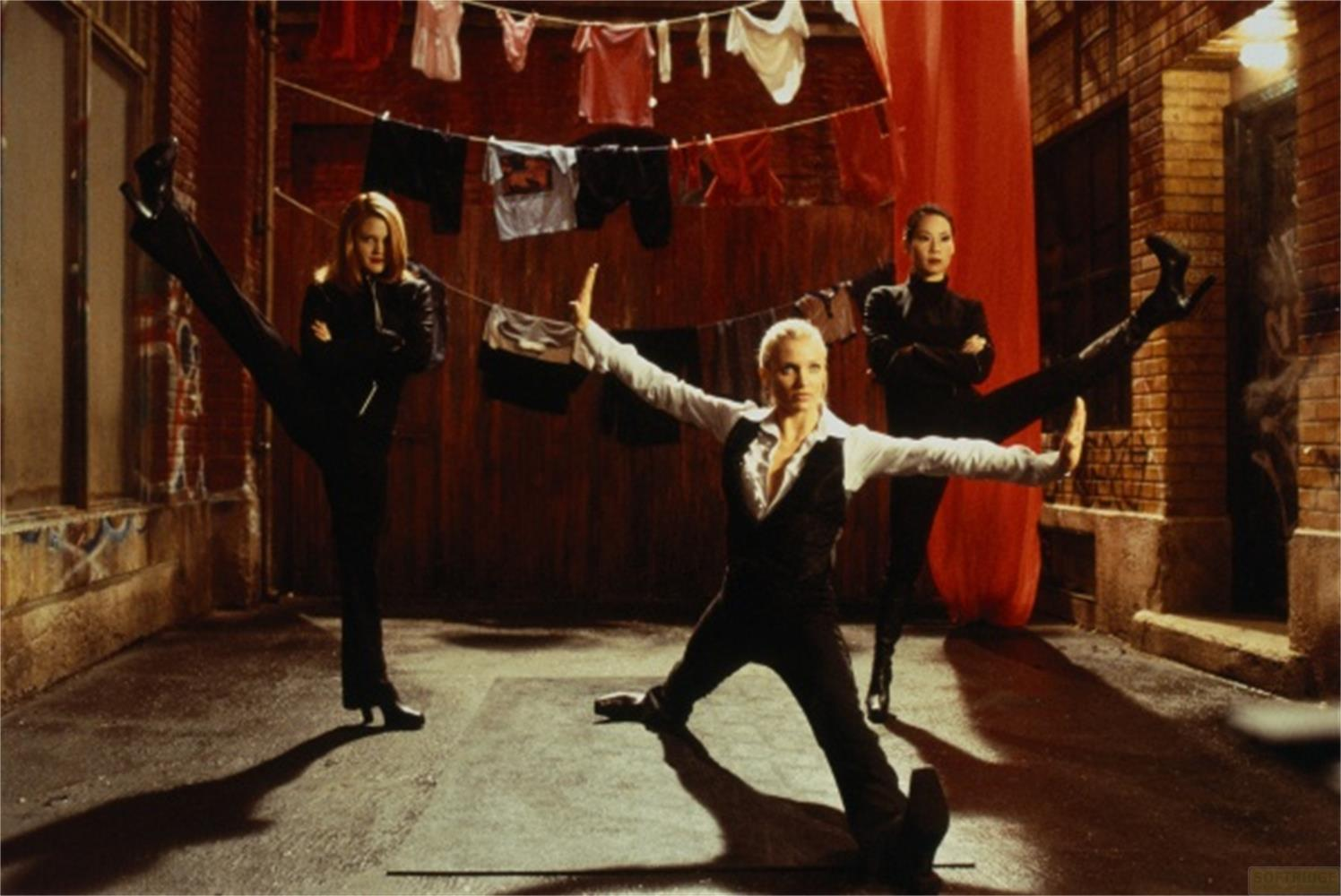 Trois femmes en poses d'arts martiaux dans une ruelle avec du linge suspendu.