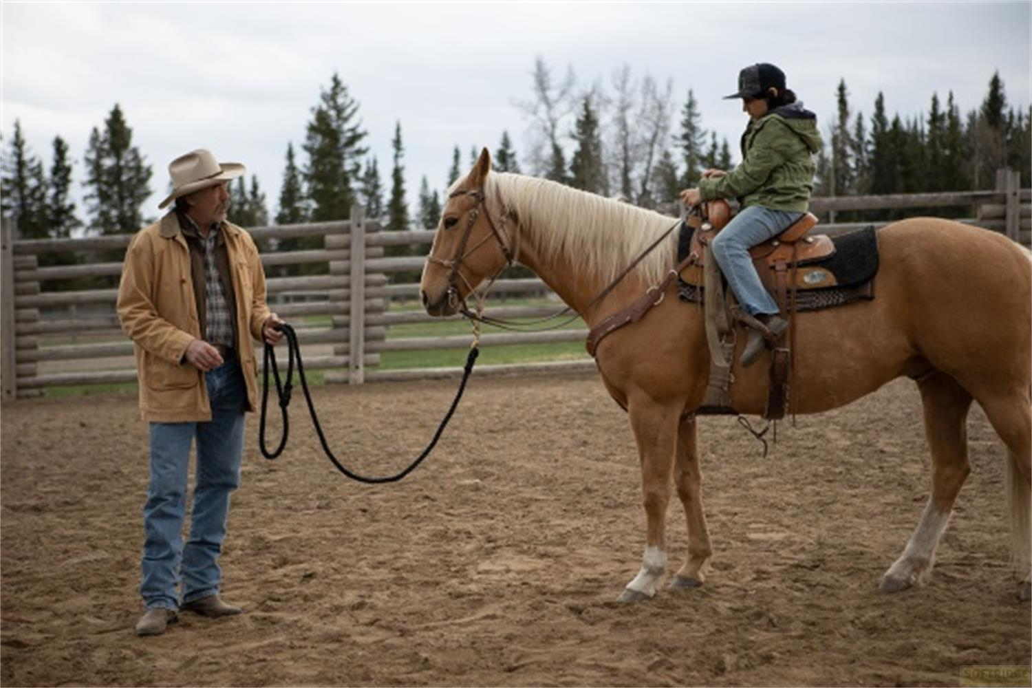 Un uomo con cappello e giacca tiene le redini. Un cavaliere siede su un cavallo.