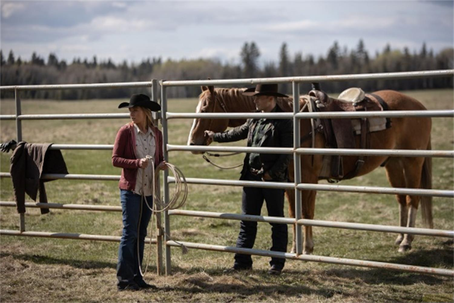 Due cowboy stanno dietro una recinzione accanto a un cavallo.