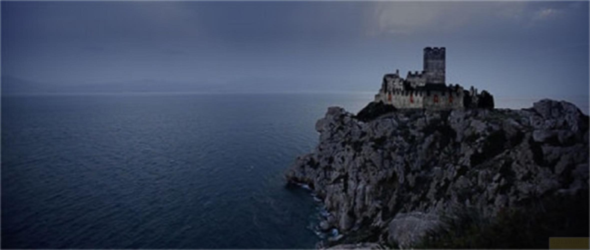 Un castello su una scogliera che domina il mare sotto un cielo drammatico.