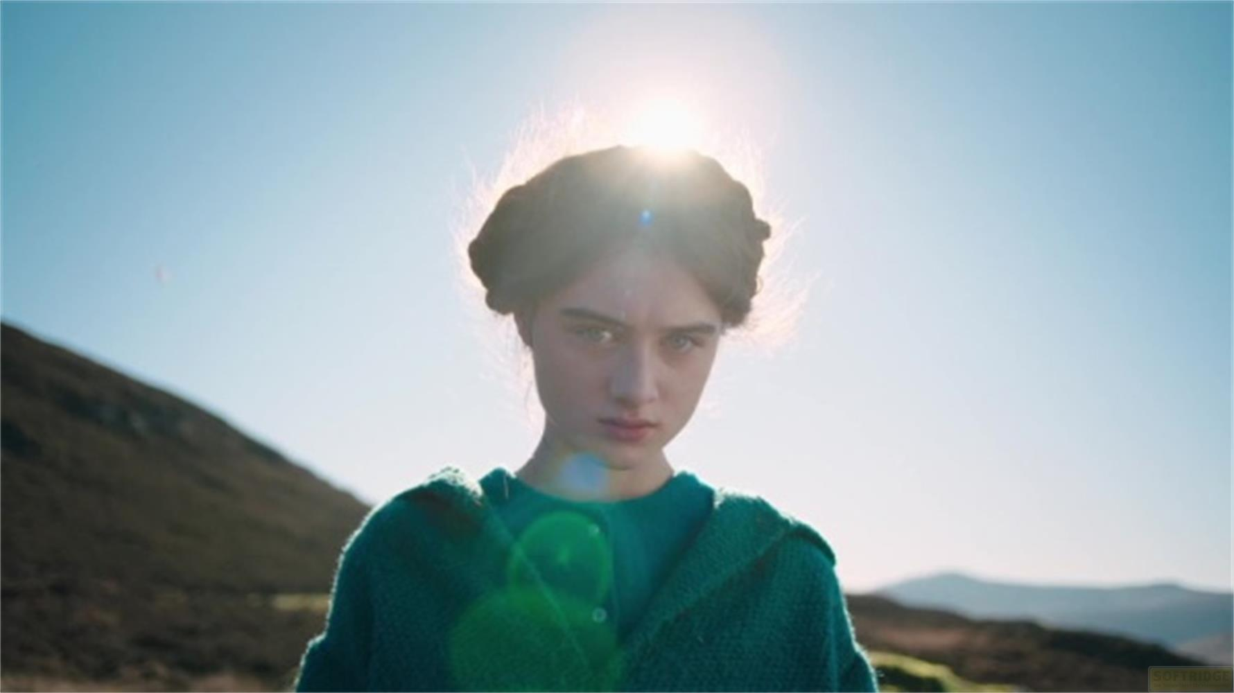 Una ragazza in maglione verde all'aperto con colline sullo sfondo.
