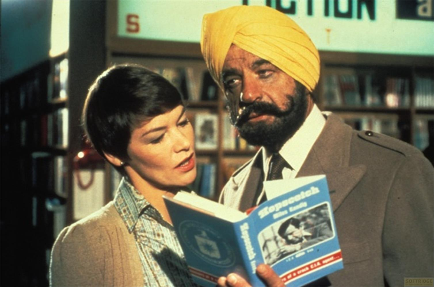 Un uomo con turbante giallo e una donna leggono un libro davanti a scaffali.