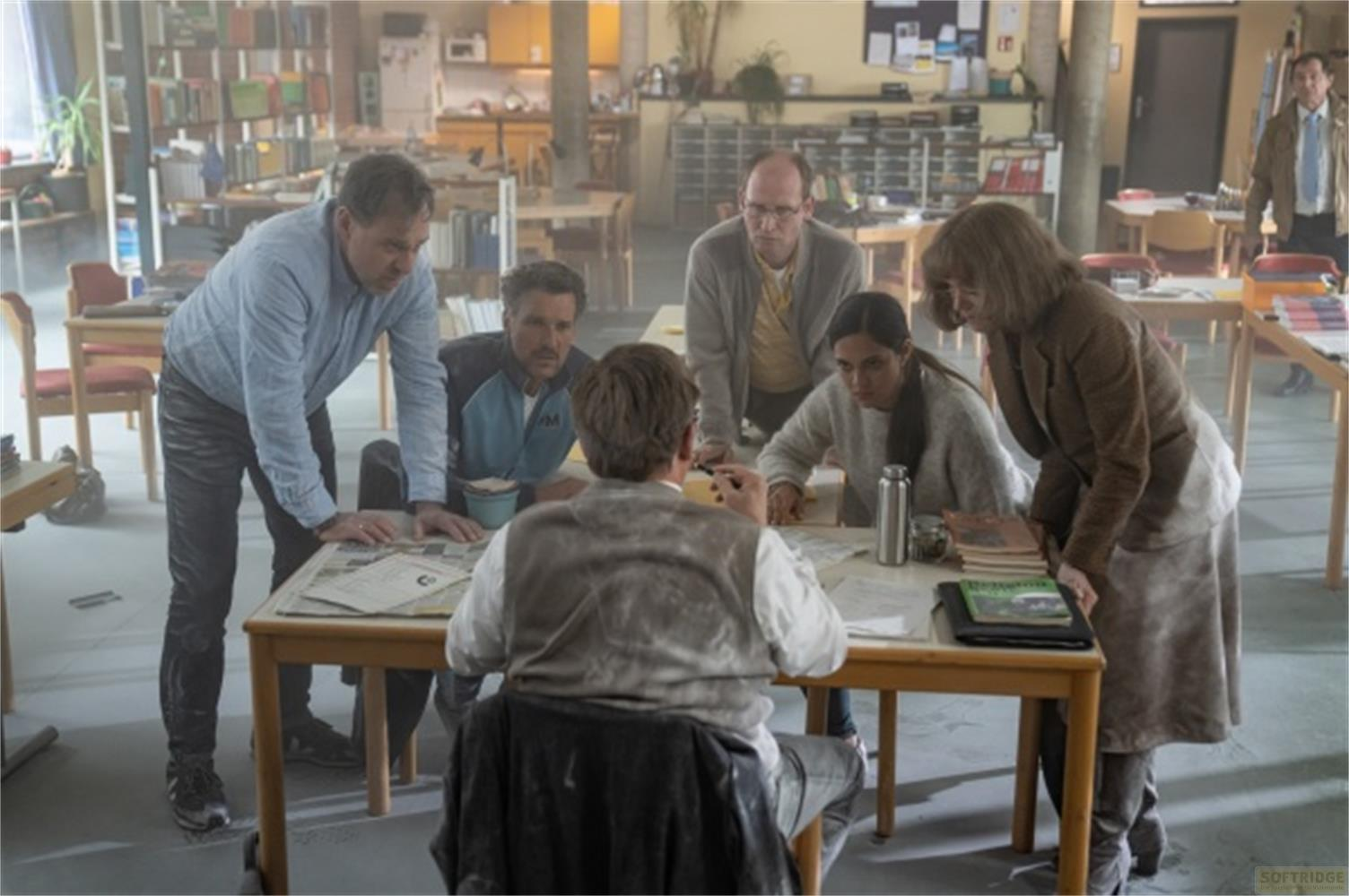 Sei persone si riuniscono attorno a un tavolo in un'aula, guardando documenti.