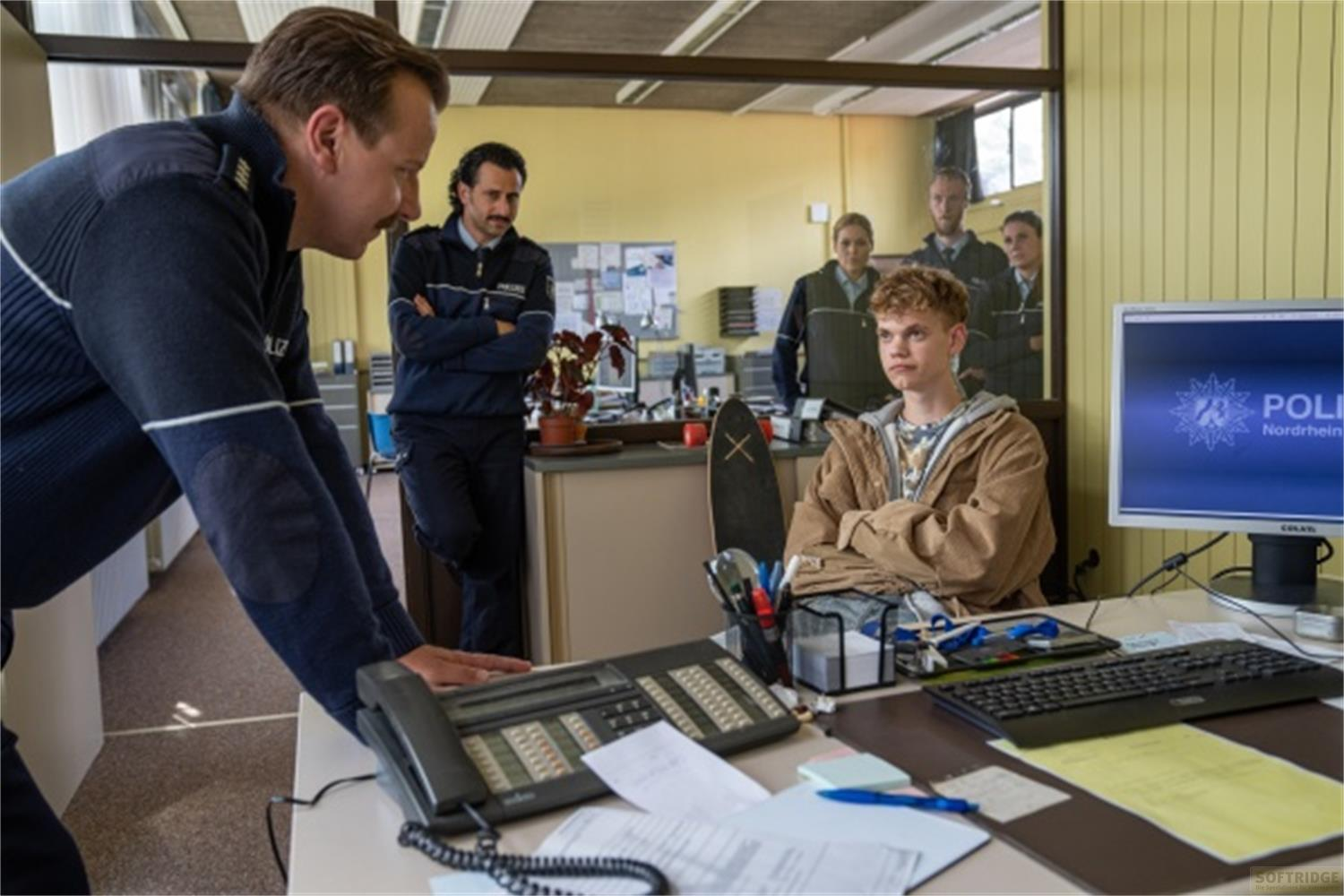 Agenti di polizia e un giovane in un ufficio. Uno guarda il computer.