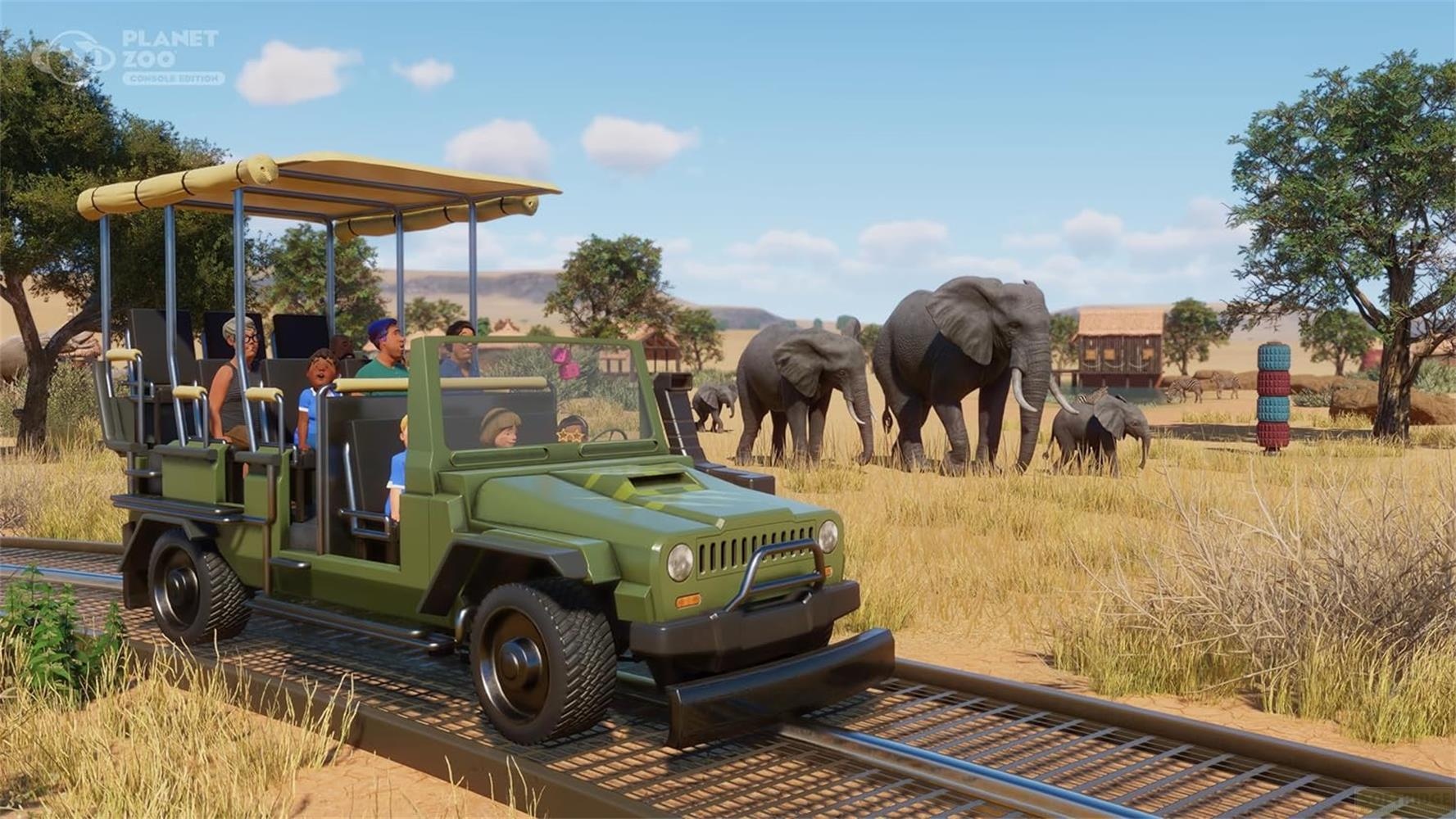 Ein grüner Safari-Jeep mit Besuchern fährt auf Gleisen, Elefanten grasen im Hintergrund.