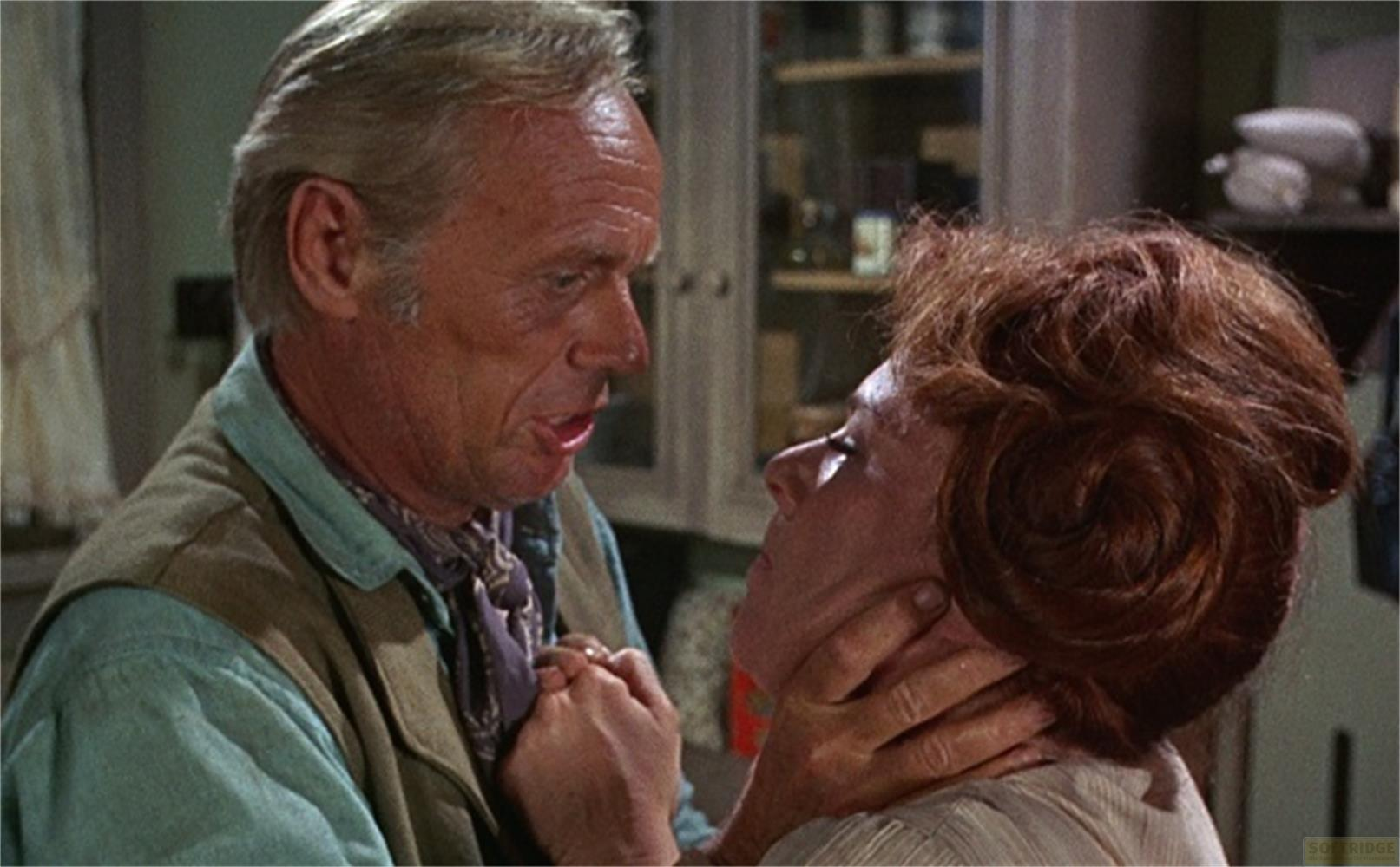 Un uomo dai capelli biondi tiene il mento di una donna. Lei lo guarda.