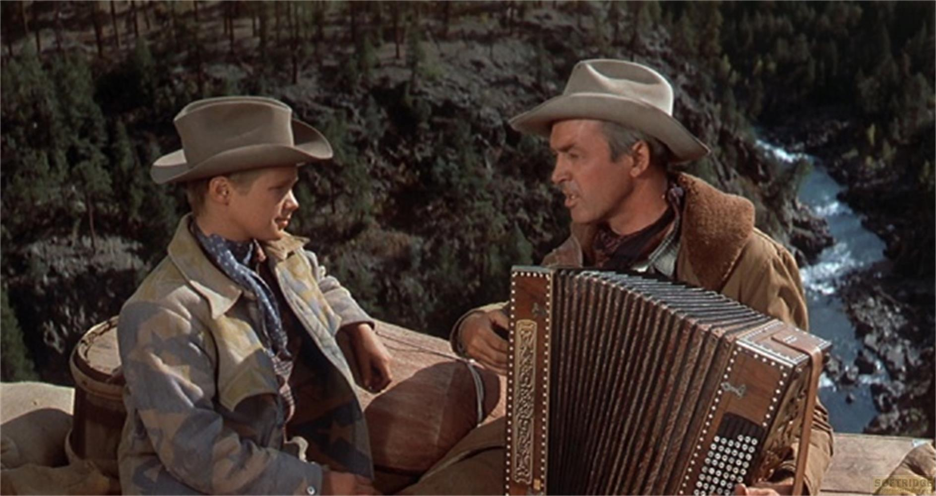 Due uomini con cappelli da cowboy siedono all'aperto, uno suona una fisarmonica.