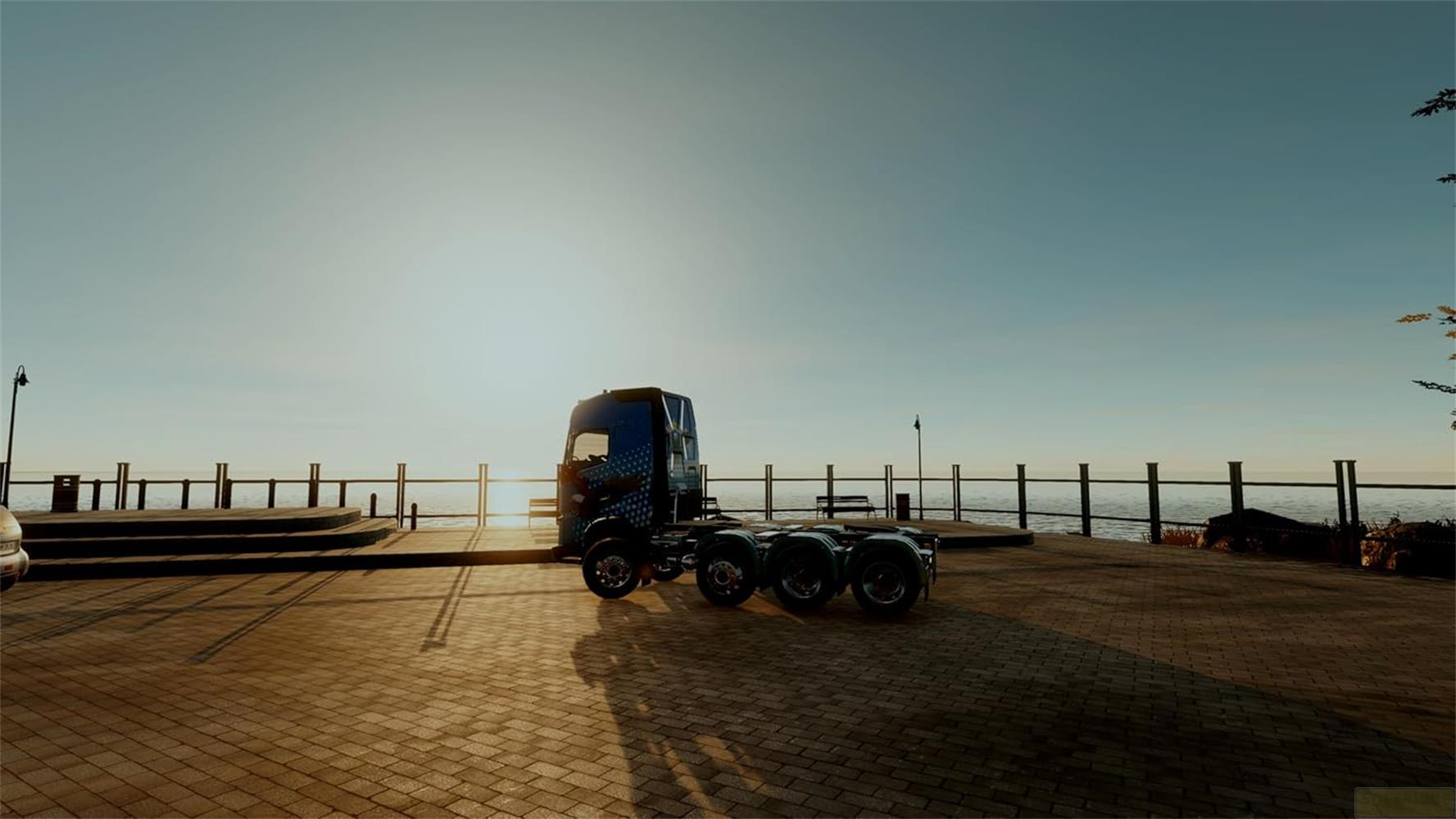 Ein blauer LKW steht am Wasser bei Sonnenuntergang auf einem gepflasterten Weg.