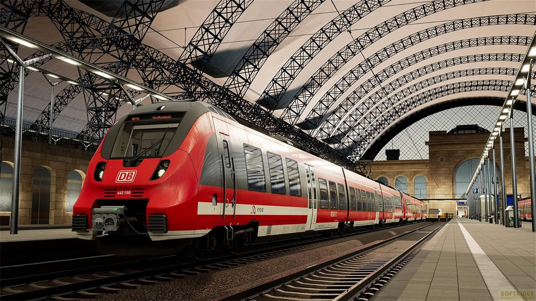 Ein roter und grauer Zug steht auf Gleisen in einer Bahnhofshalle unter einem Gitterdach.