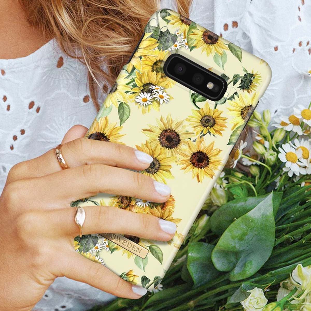 Una mano tiene un telefono con motivo di girasoli su sfondo giallo chiaro.