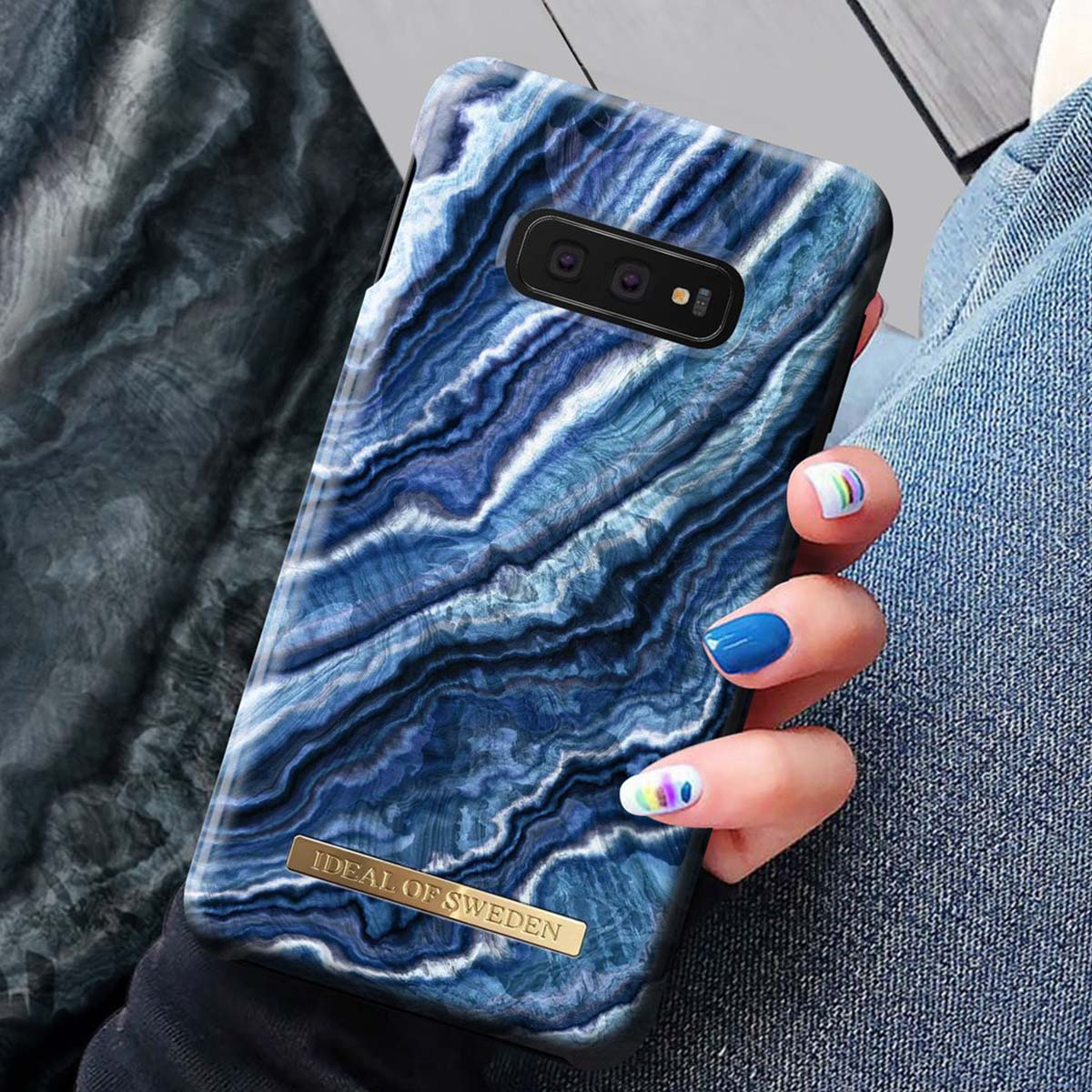 Una cover per telefono con motivo marmorizzato blu e logo dorato "Ideal of Sweden".