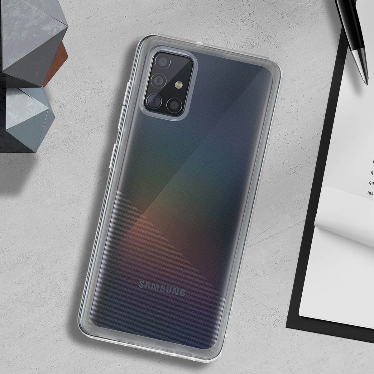 Un telefono Samsung trasparente poggia su una superficie grigia, vicino a oggetti geometrici.