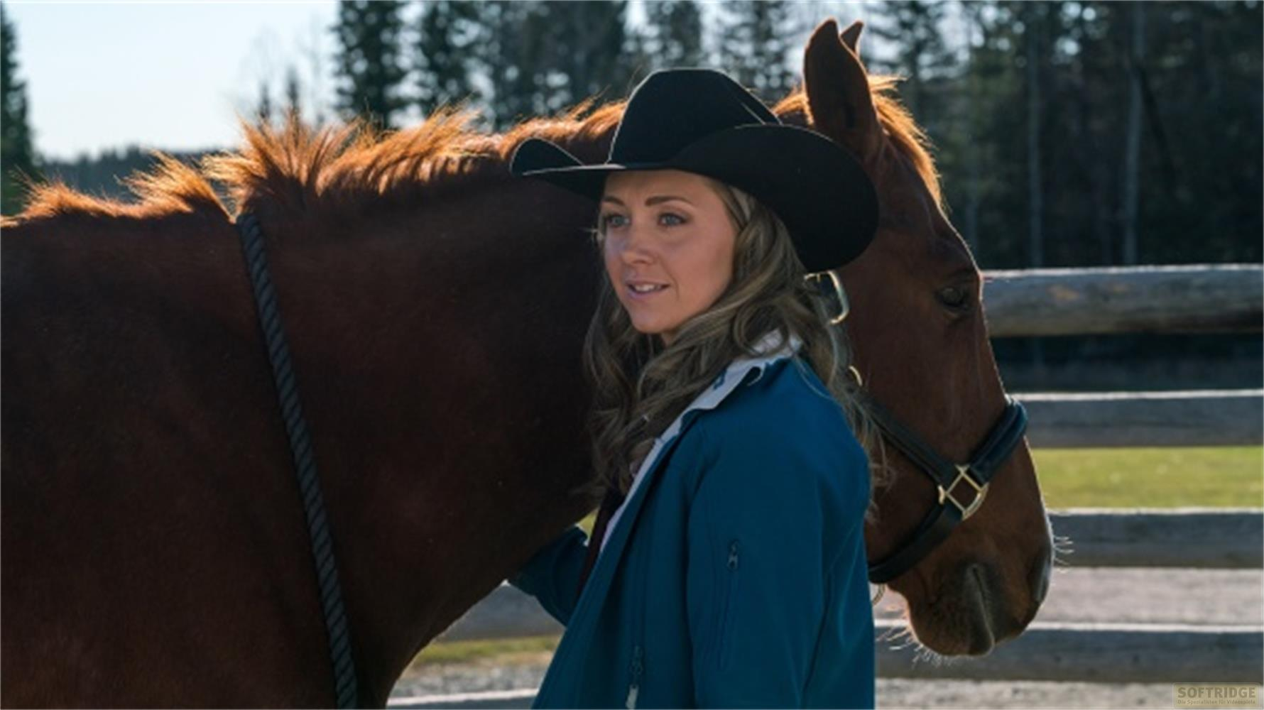 Donna con cappello da cowboy accanto a un cavallo marrone all'aperto.