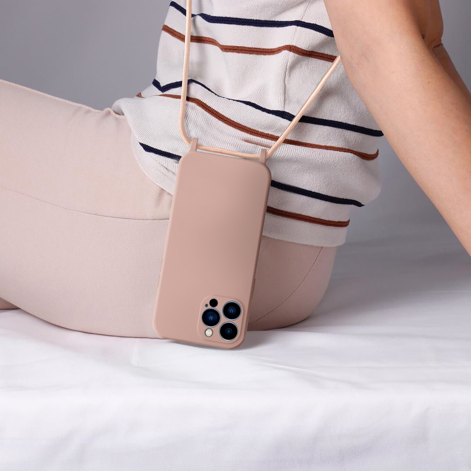 Una persona con top a righe seduta tiene un telefono rosa con laccetto.