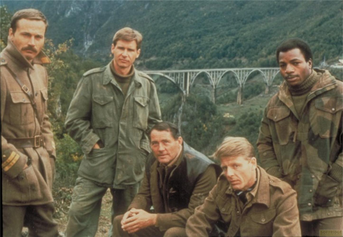 Cinq hommes en tenue militaire posent devant un pont dans les montagnes.