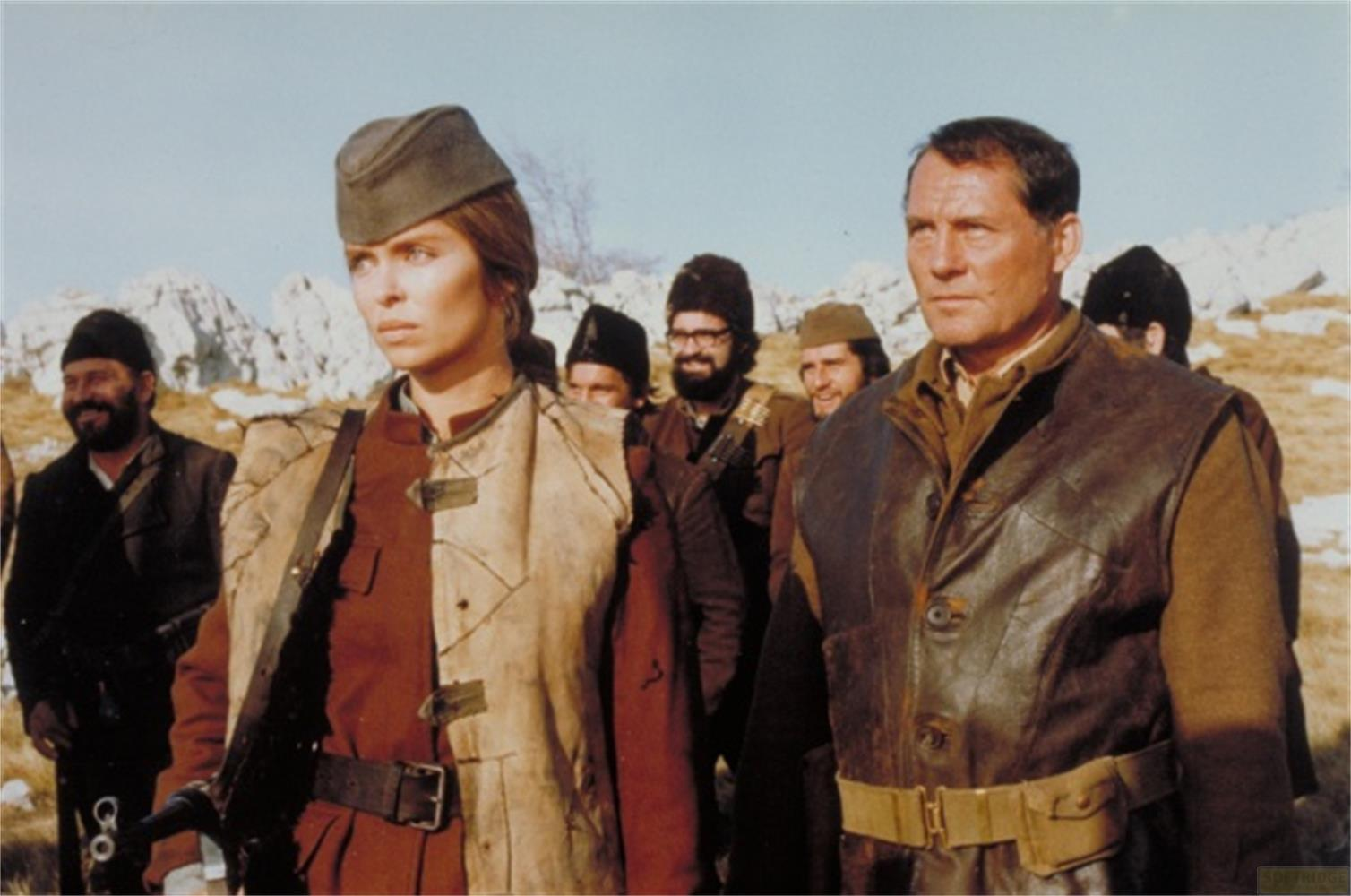 Un groupe d'hommes et une femme en uniforme se tiennent dehors. Montagnes à l'arrière-plan.