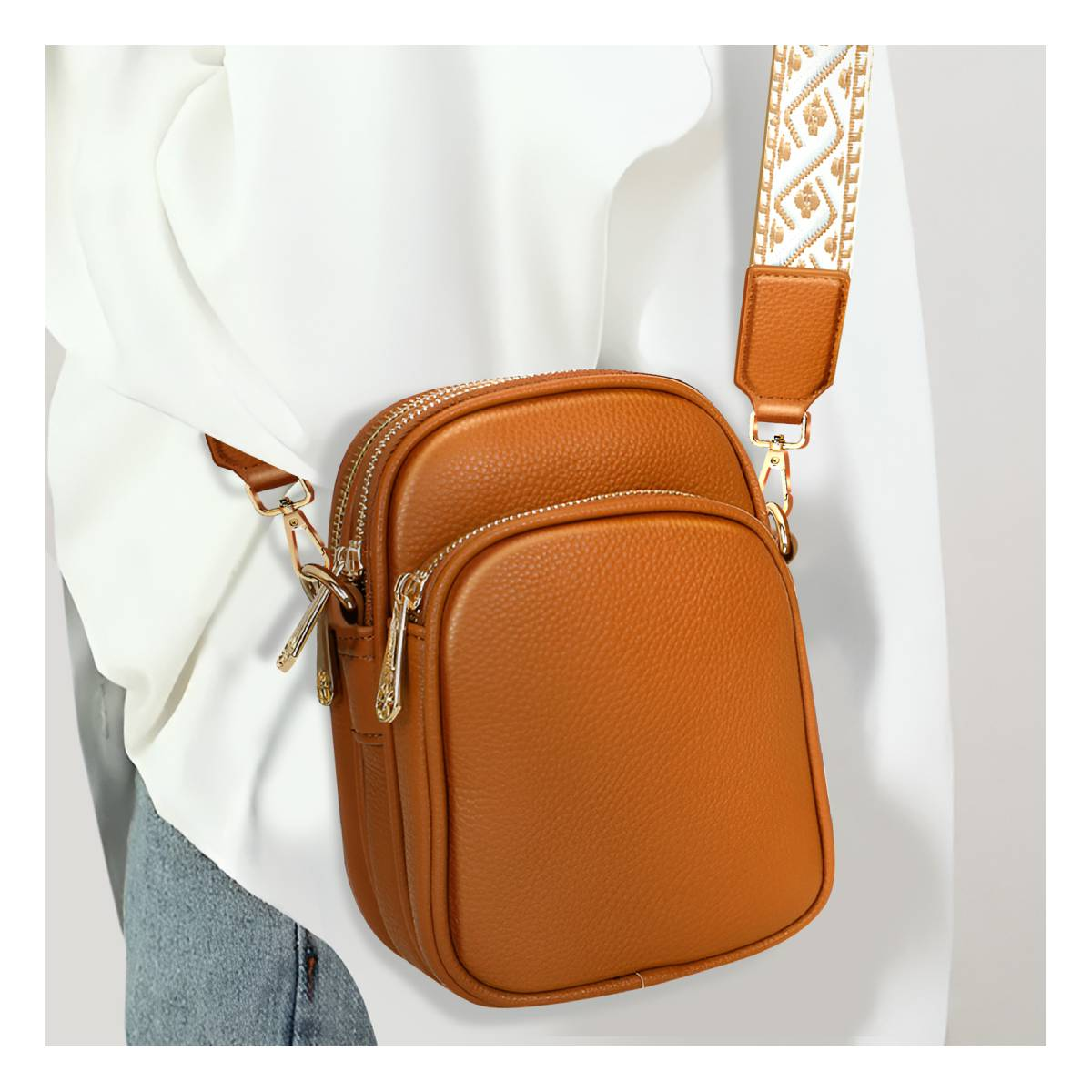 Bolso cruzado de cuero marrón con cremalleras y correa decorativa.
