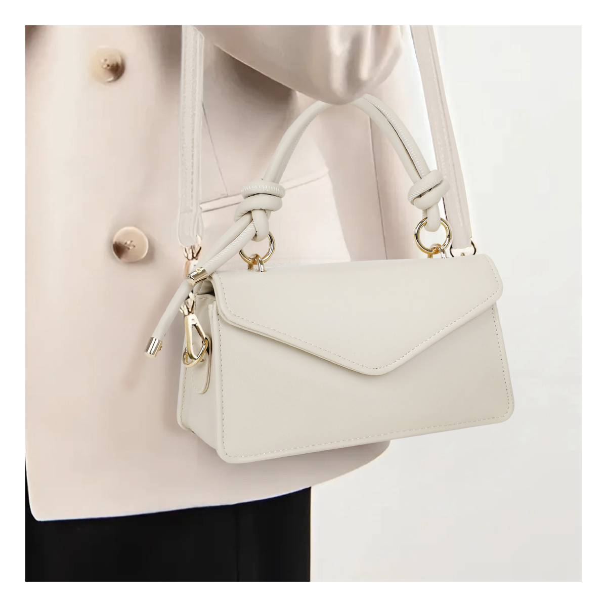 Eine weiße Handtasche mit goldenen Beschlägen wird von einer Person mit einem beigen Blazer getragen.