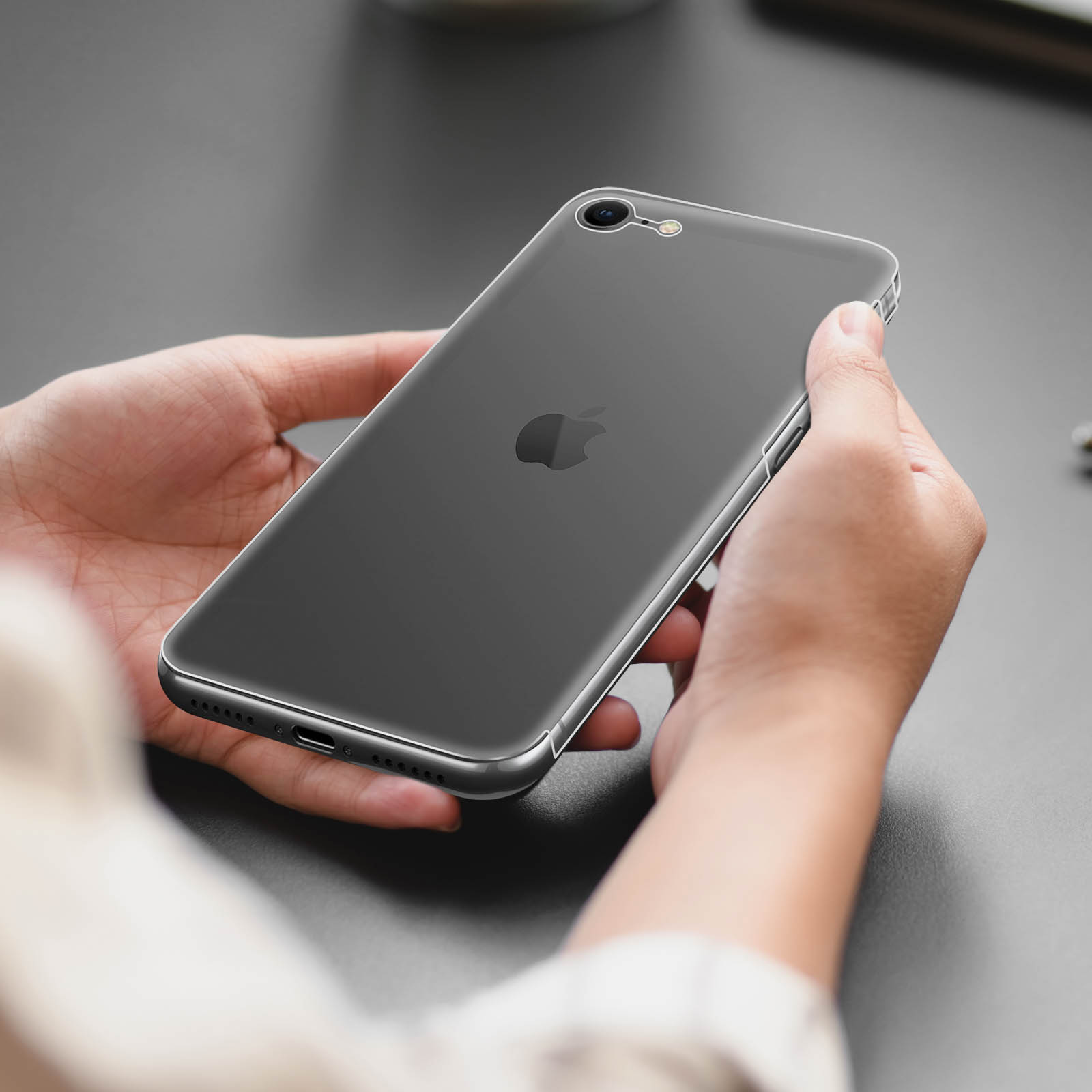 Mani che tengono uno smartphone scuro con custodia trasparente su una superficie grigia.